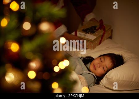 La mano di Babbo Natale che mette un regalo sotto un cuscino della ragazza addormentata Foto Stock