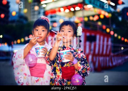 Ragazza in yukata mangiare ghiaccio rasato di fronte a yagura Foto Stock