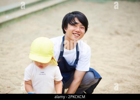 Sorridente insegnante di scuola materna e bambini che giocano nel parco Foto Stock