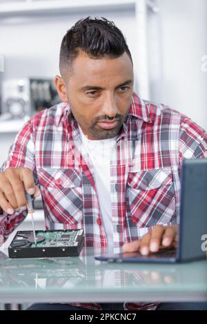 uomo che inripara un computer portatile utilizzando un cacciavite Foto Stock