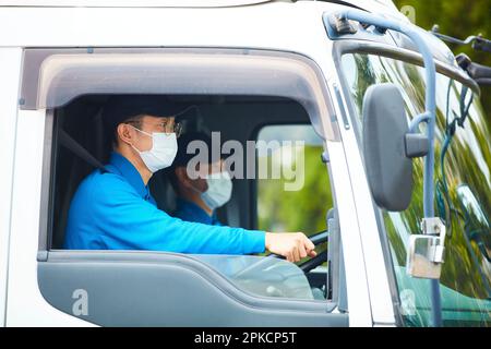 Uomo in abiti da lavoro e maschera alla guida di un camion Foto Stock