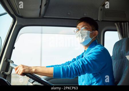 Uomo in abiti da lavoro e maschera alla guida di un camion Foto Stock