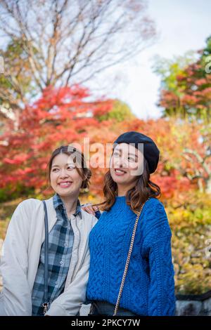 Due donne passeggiando in un luogo turistico mentre osservano le foglie autunnali Foto Stock