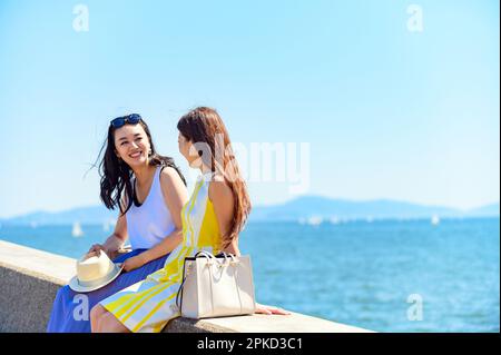 2 donne che viaggiano in un resort sul mare seduto sul frangiflutti del porto Foto Stock