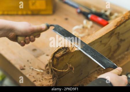 Concetto di legno di sagomatura. Lavoratore del legno professionista che usa il drawshave con entrambe le mani per modellare il pezzo di legno. Primo piano. Foto di alta qualità Foto Stock