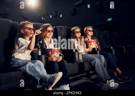 Con popcorn. Gruppo di bambini seduti al cinema e che guardano un film insieme Foto Stock