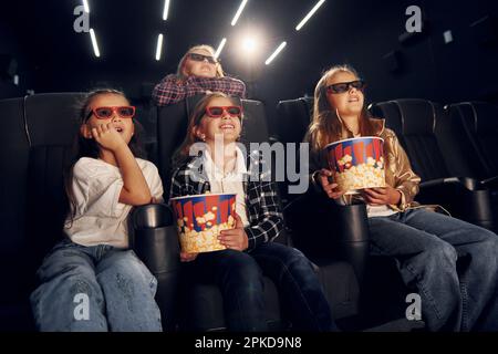 Con popcorn. Gruppo di bambini seduti al cinema e che guardano un film insieme Foto Stock