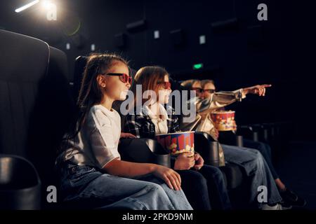 Con popcorn. Gruppo di bambini seduti al cinema e che guardano un film insieme Foto Stock