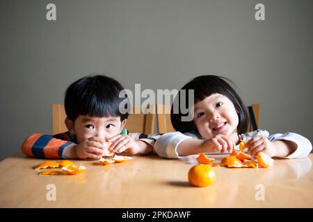 I bambini ridono mentre si pelano i tangerini Foto Stock
