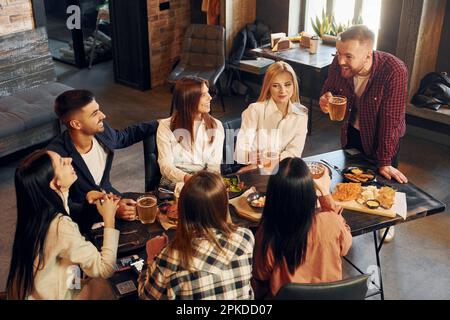 Buon umore. Gruppo di giovani amici seduti al bar con birra Foto Stock