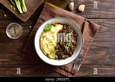 Purè di patate con manzo cotto a fuoco lento in ciotola su sfondo di legno. Vista dall'alto, disposizione piatta Foto Stock