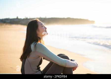 Donna in muta seduta a Sandy Beach Foto Stock