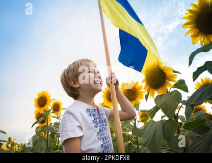 Felice ragazzo in T-shirt nazionale ricamata con bandiera giallo-blu si erge tra i girasoli in fiore. Simbolo del paese, fieri di essere ucraino. patriot Foto Stock