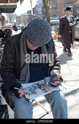 Un uomo ebreo in un berretto dipinge immagini della vita ebraica su Lee Avenue a Williamsburg, poco prima di Passover 2023. A Brooklyn, New York. Foto Stock