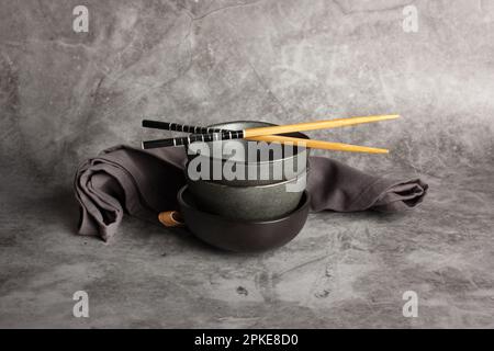 Ciotole e bacchette nere e grigie su un banco da cucina in pietra grigia con spazio copia Foto Stock