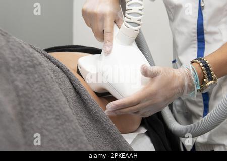 Una massaggiatrice con guanti in plastica che applica trattamenti con dispositivi per trattamenti estetici sul dorso di un paziente Foto Stock