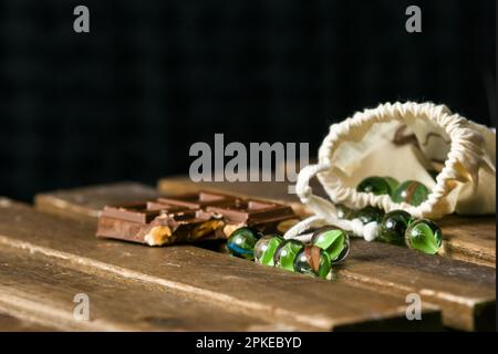 Immagine di marmi di vetro per giochi per bambini e una tavoletta di cioccolato con nocciole su un tavolo di legno Foto Stock