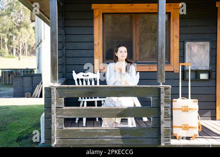 Donna bere tè sul portico di cottage Foto Stock