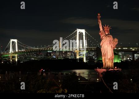 Famosa Statua della libertà storica che tocca il cielo notturno di Odaiba, Tokyo, Giappone, con lo sfondo del ponte arcobaleno. Foto Stock