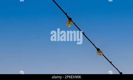 Gruppo di lampadine appese sui fili contro il cielo blu. Foto Stock