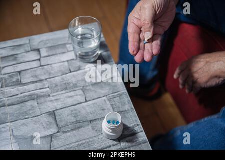 Mani di un anziano che prende la medicina a casa, sta tenendo una pillola. Foto Stock