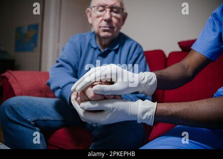 Un medico tiene le mani del paziente a casa durante una visita, concetto di unità e di convivenza. Foto Stock