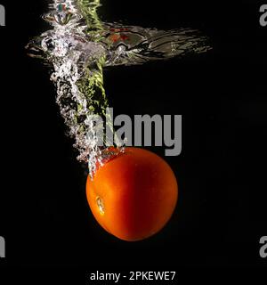 Pomodoro maturo cade profondamente sotto l'acqua con un grande splash. Foto Stock