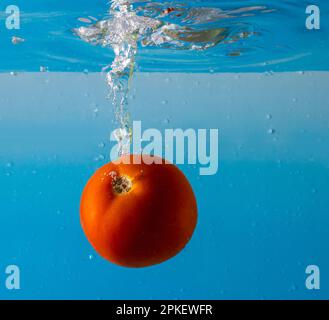 Pomodoro maturo cade profondamente sotto l'acqua con un grande splash. Foto Stock