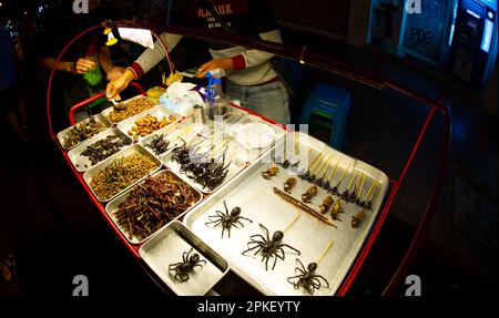 Febbraio 24 2023-Bangkok Thailandia-ragni, scorpioni, scarafaggi, locuste fritti in padelle e esposti per la vendita in una strada affollata nel centro Foto Stock
