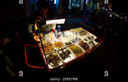 Febbraio 24 2023-Bangkok Thailandia-ragni, scorpioni, scarafaggi, locuste fritti in padelle e esposti per la vendita in una strada affollata nel centro Foto Stock