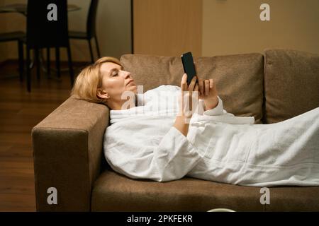 Calma donna di mezza età si trova sul divano in un accappatoio Foto Stock