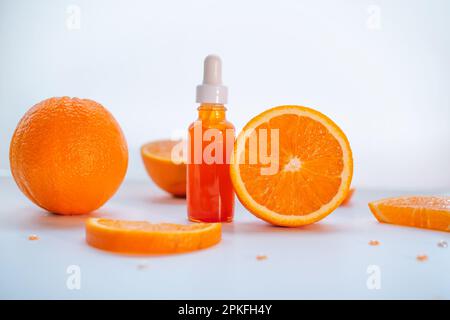 Concetto cosmetico di cura della pelle della vitamina C - siero organico in una bottiglia e fette arancioni su fondo bianco. Foto Stock