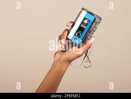 Crop anonima mano afro-americana che mostra una cassetta audio vintage su sfondo beige Foto Stock