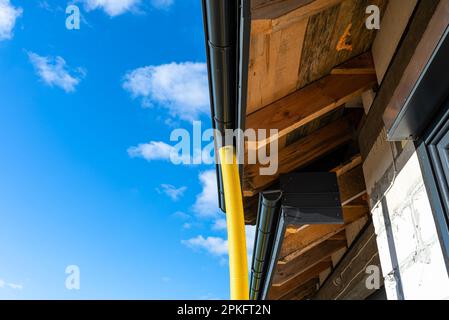 Tubo in PVC giallo con diametro di 100mm mm collegato all'estremità della canaletta sul tetto, protetto dall'acqua. Foto Stock