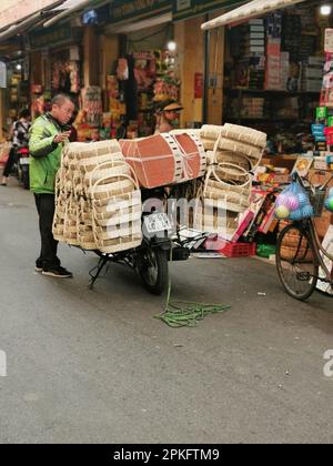 Hanoi, Vietnam. 26th Feb, 2023. Un uomo si trova accanto al suo ciclomotore pieno di carica in una strada nel centro storico. Credit: Alexandra Schuler/dpa/Alamy Live News Foto Stock