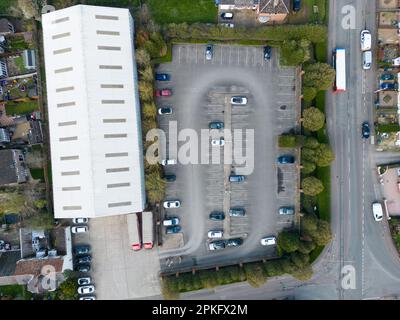 Vista dall'alto del drone di un magazzino che mostra il grande parcheggio adiacente. Una strada principale si trova sulla destra passando per il centro del paese. Foto Stock