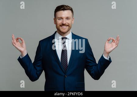 Persone d'affari consapevoli. Felice ceo esecutivo in tuta facendo esercizio di yoga, uomo d'affari di successo tenendo le mani in mudra e meditando, sorridendo a camma Foto Stock