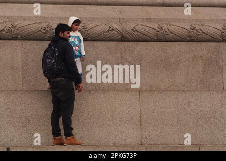 Un giovane ragazzo asiatico e suo padre in piedi sul plinto che circonda la colonna di Nelson a Trafalgar Square, Londra, Inghilterra. REGNO UNITO Foto Stock