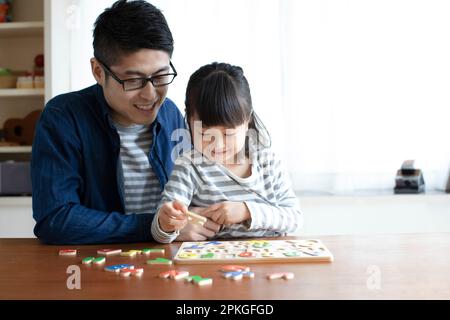 Ragazza che fa il puzzle dell'alfabeto e suo padre la aiuta Foto Stock