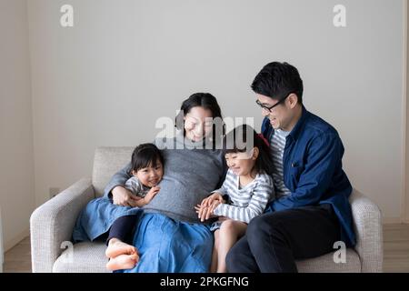 Suore e padre che coccola sul ventre di una madre incinta Foto Stock