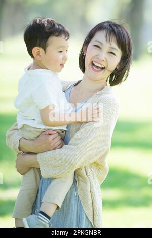 Una madre che tiene e sorride il bambino in una fila di alberi di pioppo Foto Stock