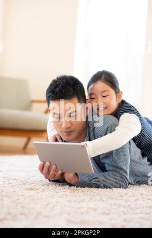 Genitore e bambino sdraiati sul pavimento guardando un tablet PC Foto Stock