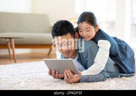 Genitore e bambino sdraiati sul pavimento guardando un tablet PC Foto Stock