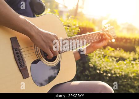 Primo piano della mano maschile che suona la chitarra contro la luce solare durante la mattina nel parco. Immagine con messa a fuoco selettiva Foto Stock