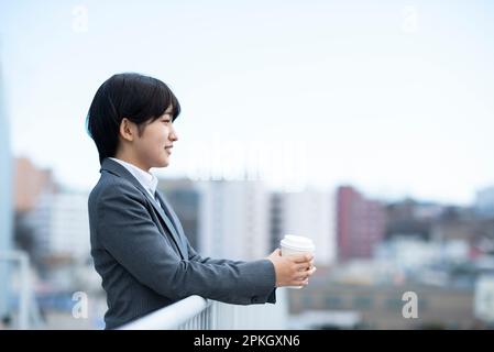 Donna d'affari che tiene il caffè e sorridente Foto Stock