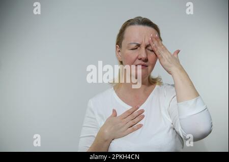 Stravolgimento stressato donna anziana tiene la testa con le mani sedersi sul divano vicino al notebook, soffre di forte mal di testa grave, emicrania cronica dopo l'uso del dispositivo, sovraccarico di informazioni, terribili notizie, debito bancario Foto Stock