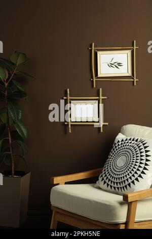 Belle foto in bambù cornici su parete marrone ed elegante poltrona al coperto. Design degli interni Foto Stock