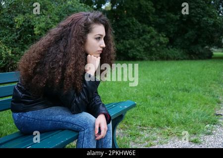 Triste adolescente femmina seduto su una panchina nel parco Foto Stock