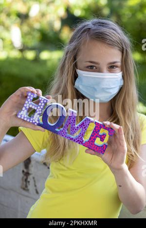 Ragazza (11) con protezione bocca-naso e scritta Home, Kiel, Schleswig-Holstein, Germania Foto Stock