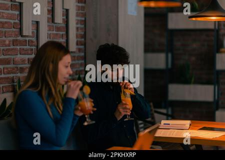 Coppia simpatica seduta insieme al caffè, sorridente parlando e bevendo i loro cocktail al caffè Foto Stock